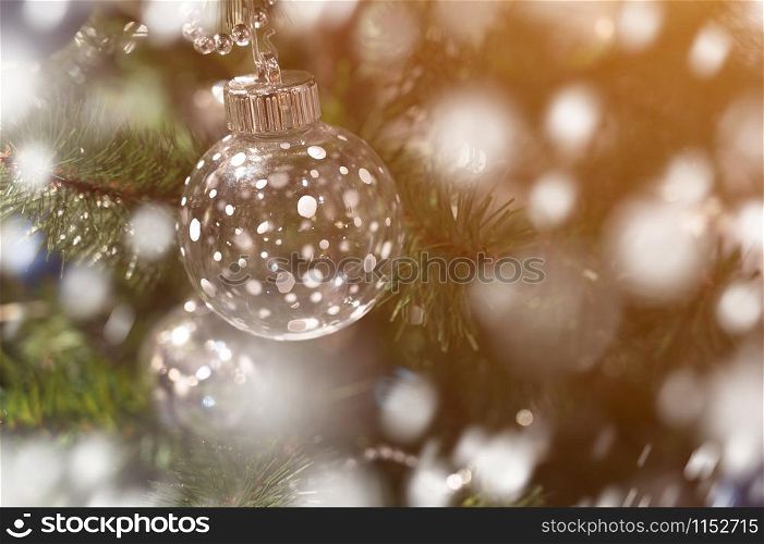 Close-up decorated Christmas pine tree with clear plastic snow ball. Copy space wallpaper with snowfall effect. Christmas and New Year holidays concept.