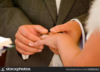 Close up detail of groom putting wedding ring on bride&acute;s finger during real ceremony