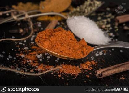 Close up detail of various spices spoons on stone slate table.