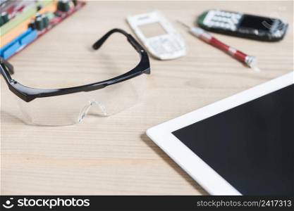 close up digital tablet safety glasses broken mobile phone wooden background