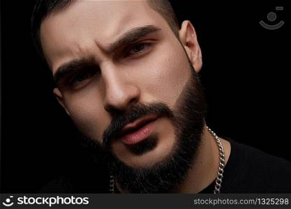 close-up dramatic portrait of a young serious discontented guy, musician, singer,rapper with a beard on a black isolated background.