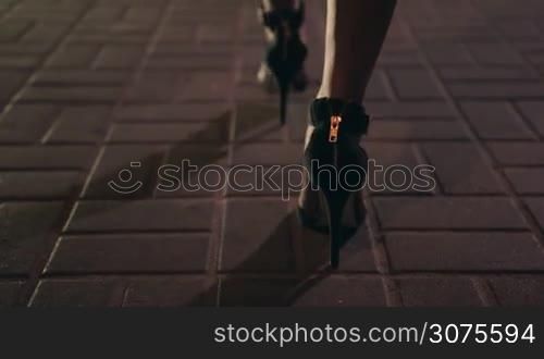 Close up elegant woman&acute;s legs on high heel shoes walking away on city street at night. Background night city lights