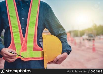 Close up engineer holding hard hat standing on road construction background