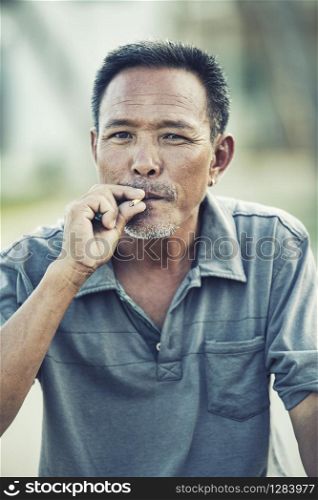 close up face of asian senior man with dry leaves cigarette looking to camera