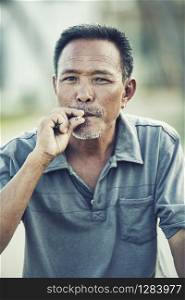 close up face of asian senior man with dry leaves cigarette looking to camera