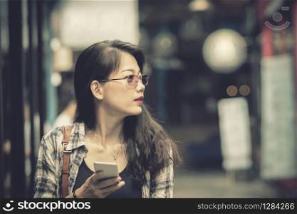 close up face of asian younger woman holding smart phone in hand walking in shopping area