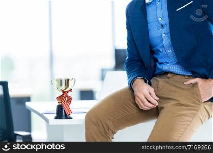 Close up fashion image of wrist in a business suit of man detail of a businessman,Man&rsquo;s hand in brown or gold pants pocket and wearing blue jacket a champion cup on table at In the office room.