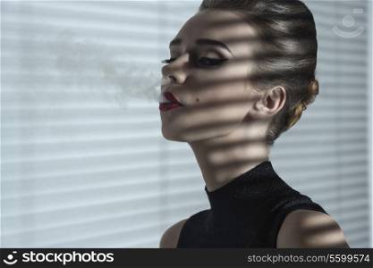 close-up fashion portrait of sexy elegant girl with stylish hair-style and make-up smoking in sensual mode in indoor atmosphere