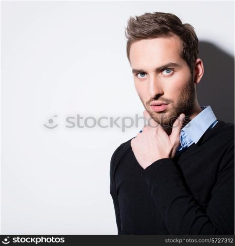 Close-up fashion portrait of young man in black pullover poses over wall with contrast shadows.