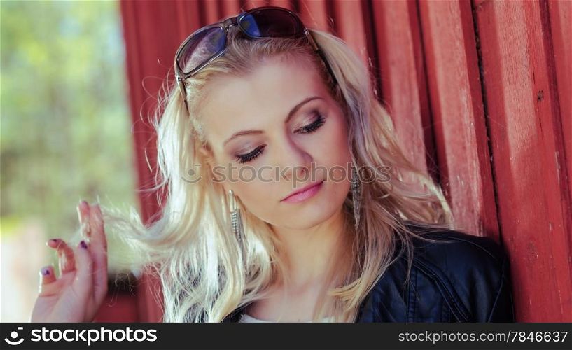 Close up, fashionable beautiful young blond wearing a leather jacket and leans against the red wall