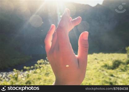 Close up female hand at sunlight outdoors concept photo. First view hand photography with summer landscape on background. High quality picture for wallpaper, travel blog, magazine, article. Close up female hand at sunlight outdoors concept photo