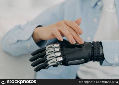 Close-up female hand touching high tech prosthetic arm. Disabled woman setting her robotic artificial limb. People with disabilities and medical technologies concept. Advertising of bionic prosthesis . Female turns on high tech prosthetic hand, artificial limb. Advertising of bionic prosthesis 