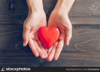 Close up female hands giving red heart on wood background