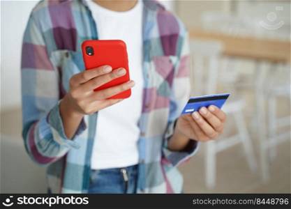 Close-up female hands holding bank credit card and smartphone, woman paying purchases, using banking services, e-bank phone apps, shopping in online store, making secure payment at home.. Female holding bank credit card, phone, uses banking services, e-bank apps, paying purchases online