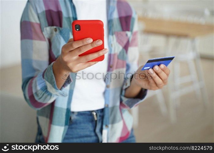 Close up female hands holding credit card and smartphone. Woman paying purchases, using online banking services, mobile bank apps, shopping on the internet, makes secure payment indoors.. Female holding credit card, phone, uses online banking services, mobile bank apps, paying purchases