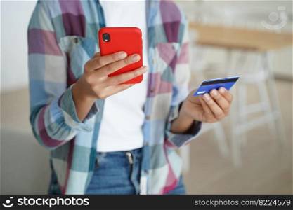 Close up female hands holding credit card and smartphone. Woman paying purchases, using online banking services, mobile bank apps, shopping on the internet, makes secure payment indoors.. Female holding credit card, phone, uses online banking services, mobile bank apps, paying purchases
