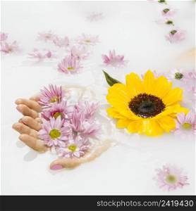 close up female s hand holding yellow pink flowers liquid background