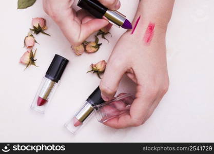 close up female testing different lipsticks hand white backdrop