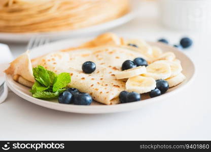 Close-up French crepes with banana and blueberries on white table
