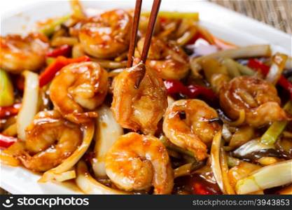 Close up front view of a curry shrimp, selective focus on single piece in chopsticks, with fresh peppers on onion in background.