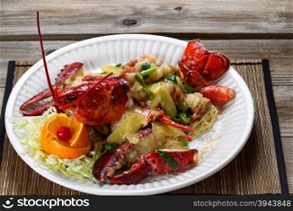 Close up front view of a freshly cooked whole Maine lobster covered with herbs, onions, and sauce on white plate.