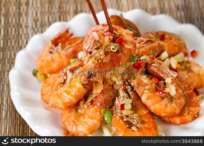 Close up front view of a fried bread coated shrimp, selective focus on single piece in chopsticks, with fresh garnishes.