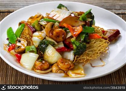 Close up front view of a fried noodle with shrimp, pork, vegetables and sauce in white plate.