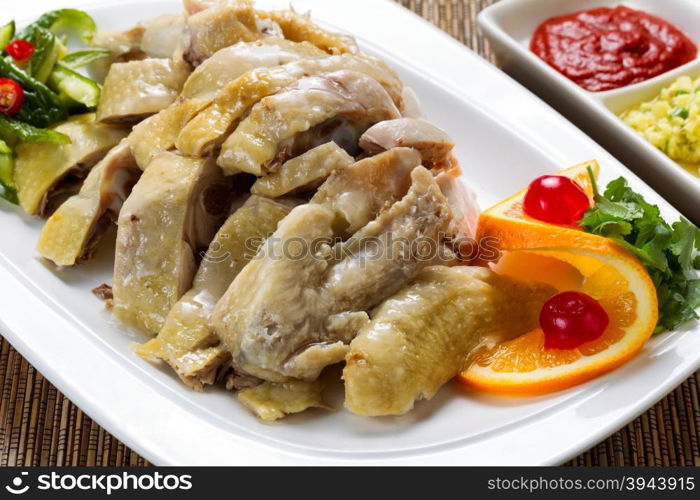 Close up front view of a succulent sliced chicken with dipping sauces and garnishes in background on bamboo mat.