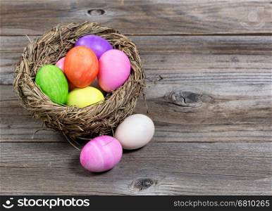 Close up front view of colorful Easter eggs in bird nest on rustic wooden boards.