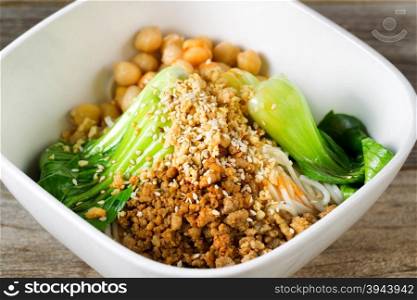 Close up front view of crispy spicy chicken with noodles and bok choy in white bowl. Selective focus in middle of dish.