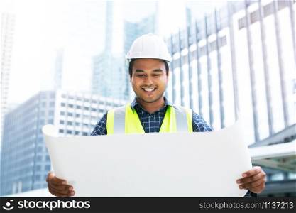 Close up front view of engineering male construction worker holding safety white helmet and wear reflective clothing for the safety of the work operation. outdoor of building background.