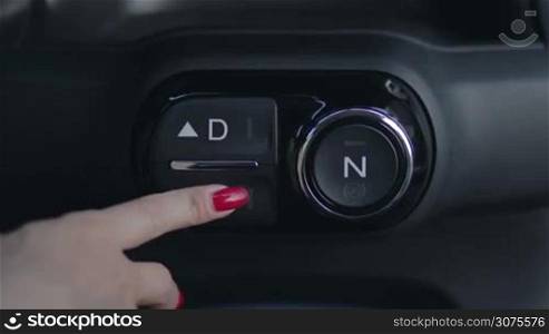 Close up front view of female hand pushing reverse gear button on car dashboard