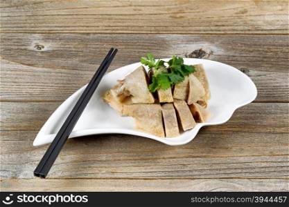 Close up front view of sliced duck meat in small bowl on rustic wood with chopsticks.
