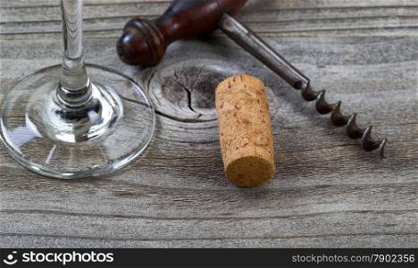 Close up front view of used cork, focus on front part of cork, with antique corkscrew and partial wine glass in background on rustic wood. Horizontal layout.