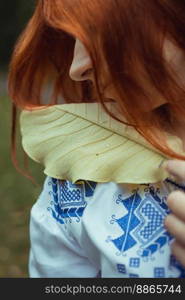 Close up ginger haired woman looking at dew drops on leaf portrait picture. Closeup front view photography with blurred background. High quality photo for ads, travel blog, magazine, article. Close up ginger haired woman looking at dew drops on leaf portrait picture