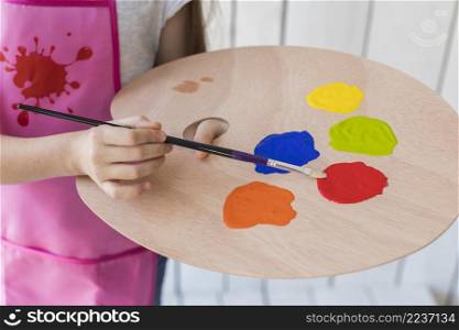 close up girl mixing paint with brush wooden palette