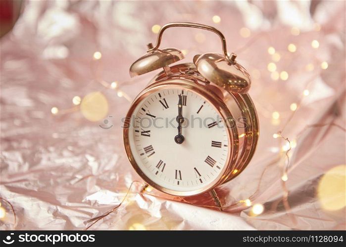 Close up golden painted alarm clock with Christmas time is midnight on a shiny cooper abstract background with garland, copy space. Greeting card.. Christmas card with golden alarmclock and garland.