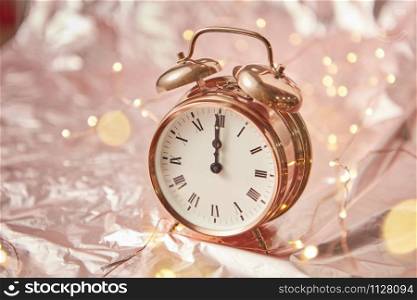 Close up golden painted alarm clock with Christmas time is midnight on a shiny cooper abstract background with garland, copy space. Greeting card.. Christmas card with golden alarmclock and garland.