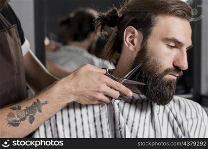 close up hairdresser cutting male customer s beard
