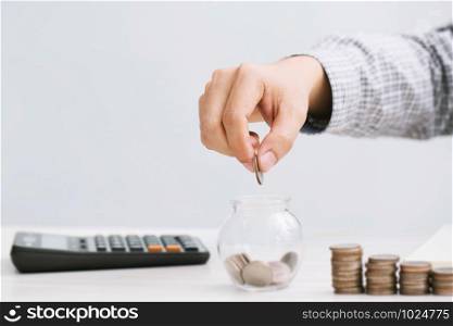 close up hand business man accounting calculator with savings money coins stacked row with hand putting coins in jug glass. concept Write Finance accounting.