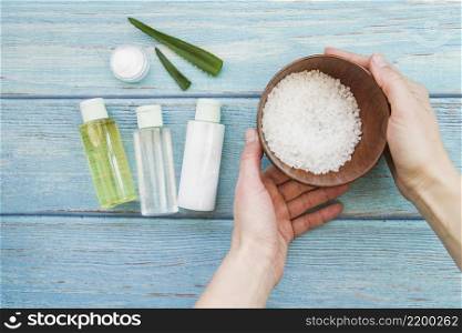 close up hand holding bowl rock salts with aloevera spray bottles cream
