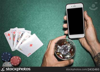close up hand holding cellphone whisky glass poker table