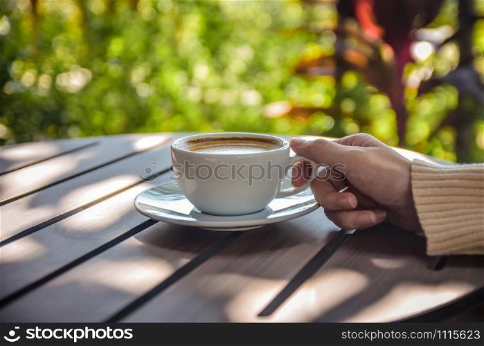 Close up hand holding cup of coffee on wooden table