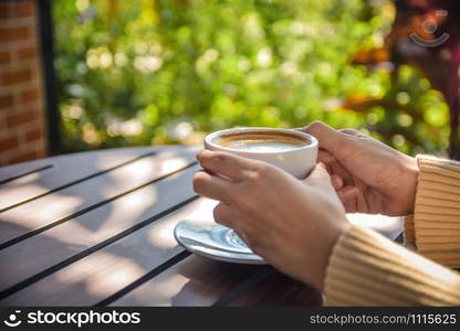 Close up hand holding cup of coffee on wooden table