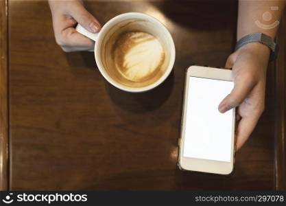 Close up hand holding mobile with empty white screen and coffee cup on table. Business and technology concept.