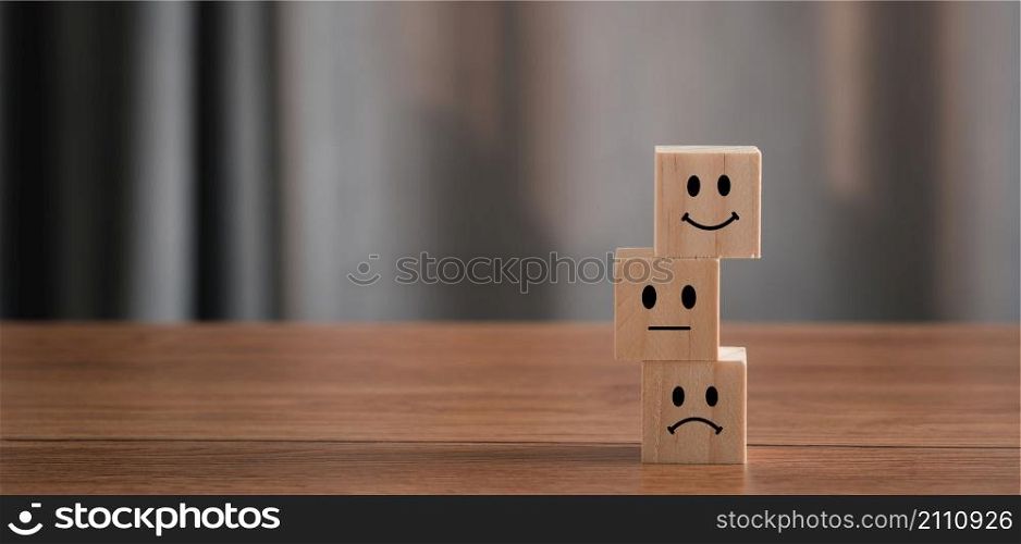 Close up Hand holding of Happy icon on cube blocks about service rating feedback of survey from customer. Business annual satisfaction survey concept. Many sad or happily on wooden table. copy space