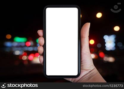 Close-up hand holding phone vertical, Using smart phone towards blurred traffic light at night background - copy space.