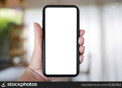 Close-up hand holding phone vertical, Using smart phone with blurred background of house, cafe interior - copy space.