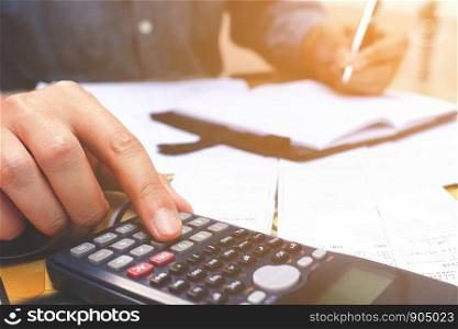 Close up hand man using calculator and make note in home office.