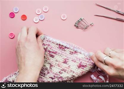 close up hand measuring knitted fabric with tape pink background
